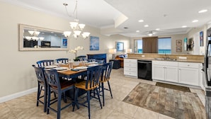 A dining area with a table set for four, a kitchen with white cabinets, and a large mirror above the counter.