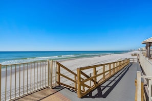Une promenade en bois qui mène à une plage, avec un ciel bleu dégagé.