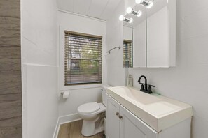A bathroom with a toilet, a sink, a mirror, and a window with blinds. - Chic City Retreat 93J - For 2! (Columbus)