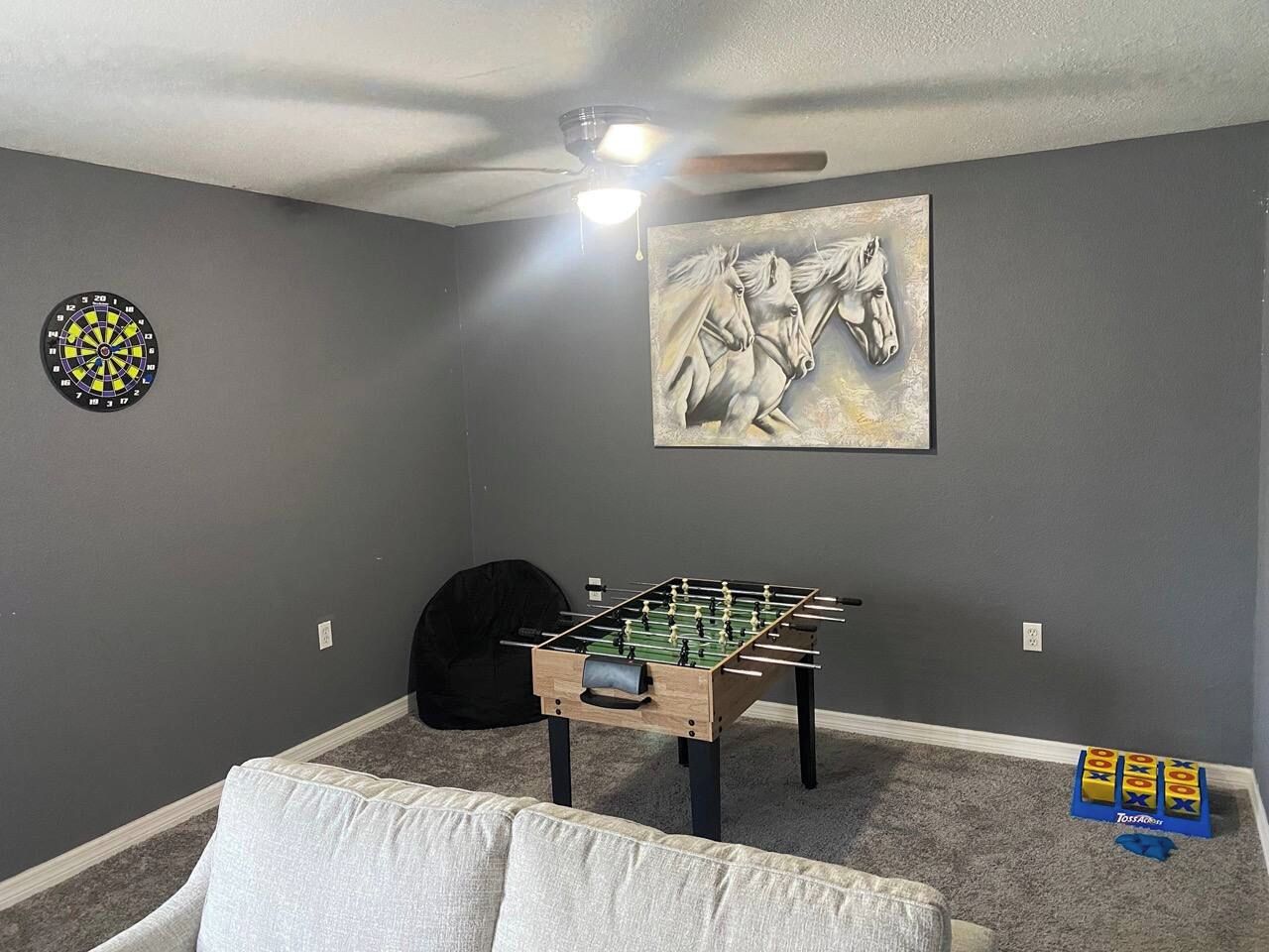 Une pièce aux murs gris, avec une table de baby-foot, un jeu de fléchettes et un tableau représentant un cheval.