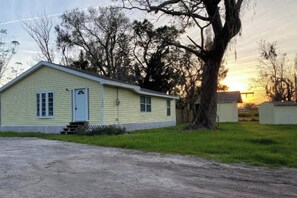 A single-story yellow building with a front door and windows, surrounded by trees and a clear sky. - Palmetto Ellenton | Nature + Smart Comfort (Palmetto)