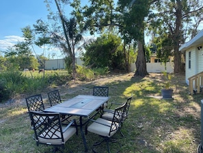 A patio with a table and chairs, surrounded by trees and a house. - Palmetto Ellenton | Nature + Smart Comfort (Palmetto)