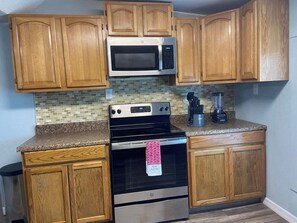 A kitchen with wooden cabinets, a stainless steel microwave, an oven, and a granite countertop. - Palmetto Ellenton | Nature + Smart Comfort (Palmetto)