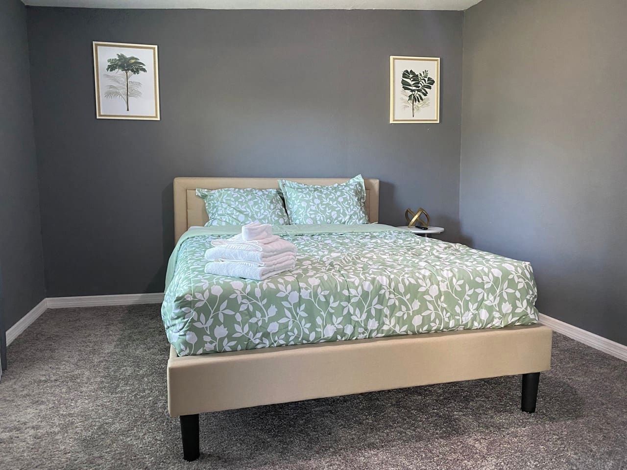 A bedroom with a bed, pillows, and two framed pictures on the wall.