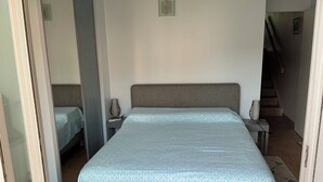 A bedroom with a large bed, a smaller bed, a nightstand with a lamp, and a staircase in the background. - Appartement Le Lavandou centre (Le Lavandou)