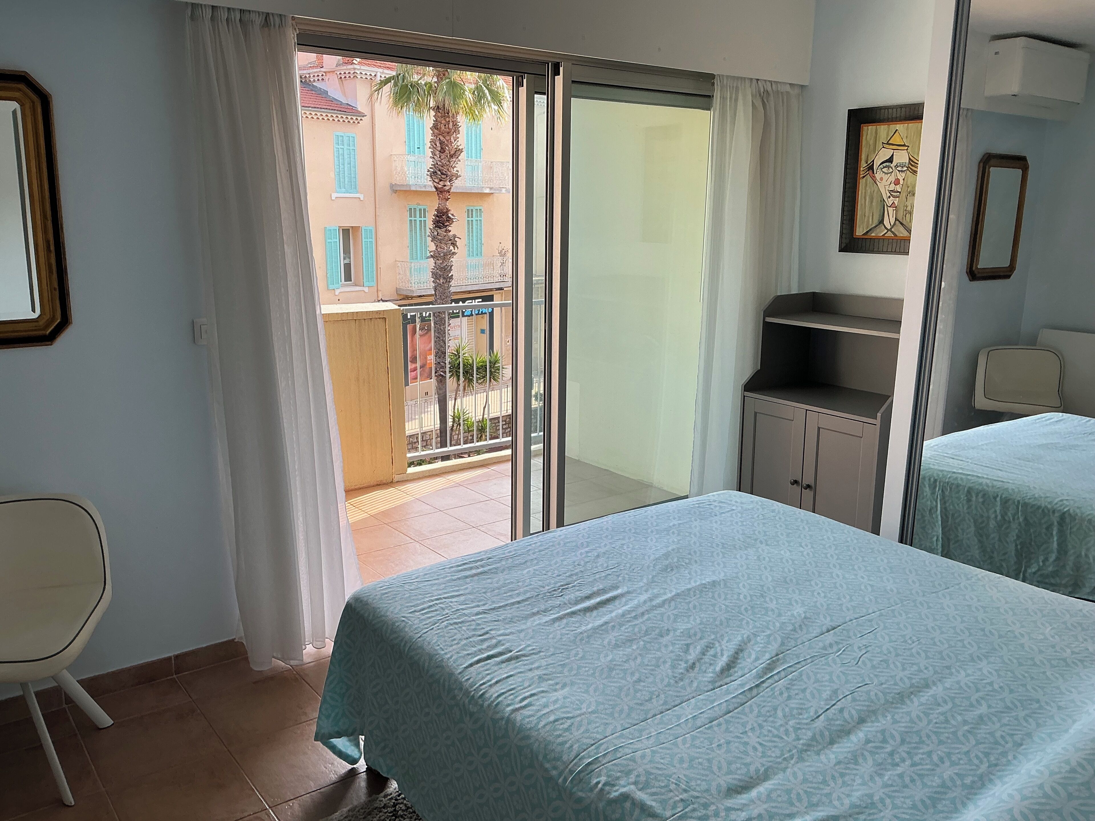 A hotel room with a balcony, a bed, a chair, and a small cabinet.