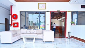 A modern lobby with a white sofa, a coffee table, a fire extinguisher, and a glass door leading to a restaurant. - HOTEL MADHUVAN & RESORT (Danta Ramgarh)
