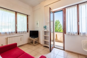 A room with a red sofa, a television on a wooden stand, a fan, and a sliding glass door leading to an outdoor area.