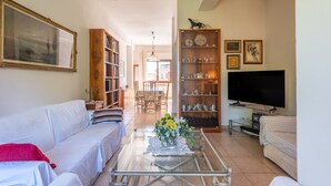 Ein Wohnzimmer mit einer Couch, einem Couchtisch mit Blumen, einem Fernseher und einem Bücherregal.