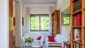 Ein Zimmer mit einer Couch, einem Couchtisch, einem Bücherregal und einem Fenster mit Vorhängen.
