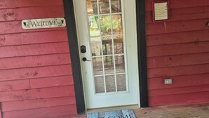 A red wooden door with a white frame and a glass panel, a welcome mat, and a sign with cabin rules.