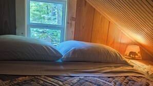 A cozy attic bedroom with a large bed, a window, and a lamp.