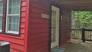 A red wooden cabin with a porch, a welcome sign, and a door.