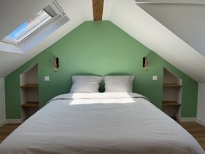 A bedroom with a sloped ceiling, a skylight, a bed with a striped bedspread, two bedside tables, and wall-mounted lamps. - Duplex apartment in Honfleur town center, a few minutes from the old port (Honfleur)