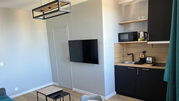 Cozinha moderna com micro-ondas, torradeira e pia. Há uma área de jantar com uma mesa posta para dois e uma TV na parede.