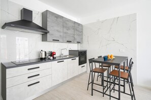 Eine moderne Küche mit einer schwarzen Dunstabzugshaube, grauen Schränken, einer Marmor-Spritzschutzwand und einem Essbereich mit Tisch und Stühlen.