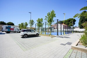 A paved area with a white car and a delivery truck, surrounded by trees and a glass enclosure.