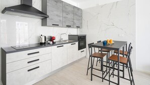 A modern kitchen with a black range hood, grey cabinets, a marble backsplash, and a dining area with a table and chairs. - GuestHost - Charming 67 sqm apartment, perfect for 4 people, located on the ground floor of a recently built building.The property is located in a residence with a concierge active all day; outside the house there are gym equipment that can be used freel (Bari)