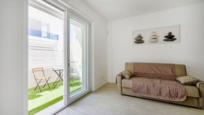 A living room with a sliding glass door leading to a balcony, a beige sofa, and a wall-mounted artwork. - GuestHost - Charming 67 sqm apartment, perfect for 4 people, located on the ground floor of a recently built building.The property is located in a residence with a concierge active all day; outside the house there are gym equipment that can be used freel (Bari)