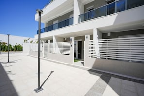 A modern multi-story building with balconies, a covered entrance, and a clear sky.