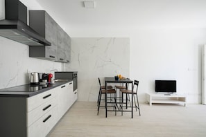 A modern kitchen with a dining area, a TV on a stand, and a marble backsplash.