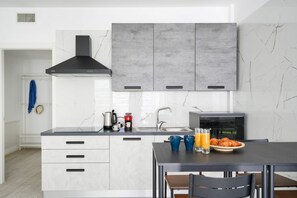 Una cocina moderna con armarios blancos, una campana extractora negra y una mesa para desayunos con croissants y zumo de naranja.