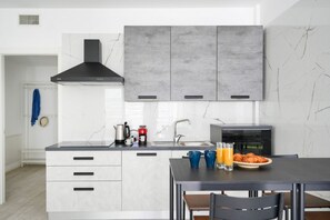 A modern kitchen with white cabinetry, a black range hood, and a breakfast setup with croissants and orange juice.