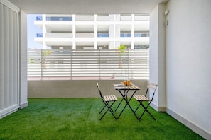 A balcony with artificial grass, a table with chairs, and a view of a modern building.