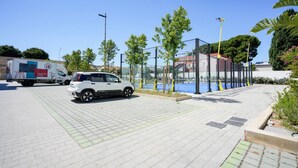 A paved area with a white car and a delivery truck, surrounded by trees and a glass enclosure. - GuestHost - Charming 67 sqm apartment, perfect for 4 people, located on the ground floor of a recently built building.The property is located in a residence with a concierge active all day; outside the house there are gym equipment that can be used freel (Bari)