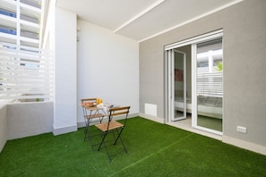 A balcony with artificial grass, a table with chairs, and a sliding glass door leading to an outdoor area.
