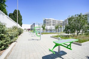 A paved walkway with exercise equipment, a green table, and a white building in the background. - GuestHost - Charming 67 sqm apartment, perfect for 4 people, located on the ground floor of a recently built building.The property is located in a residence with a concierge active all day; outside the house there are gym equipment that can be used freel (Bari)