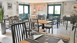Un comedor amplio con varias mesas y sillas, ventanas grandes y un diseño interior moderno.