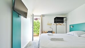 Habitación de hotel con cama, escritorio, silla, televisor y ventana con vistas a la vegetación.