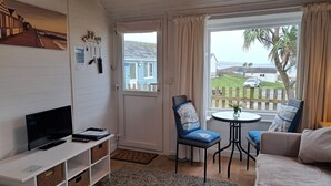 Une pièce confortable avec une télévision, une petite table avec des chaises et une vue sur l’extérieur.
