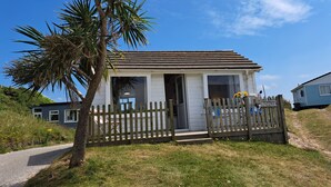Une petite maison de plain-pied, avec une clôture en bois et un palmier devant.