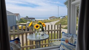 Un balcon avec une table, un vase rempli de tournesols et une vue sur la plage et les maisons.