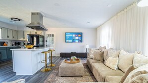 A modern living room with a kitchen island, a sofa set, and a flat-screen TV mounted on the wall. - Nutmeg (Columbus)