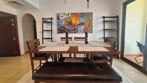 A dining area with a wooden table and benches, two hanging chandeliers, and a colorful abstract painting on the wall. - Tratoli Hostel in JBR with Sea Views (Dubai)