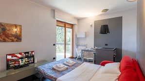 Ein Hotelzimmer mit Bett, Schreibtisch, Fernseher und einem Fenster mit Blick auf Grünflächen.