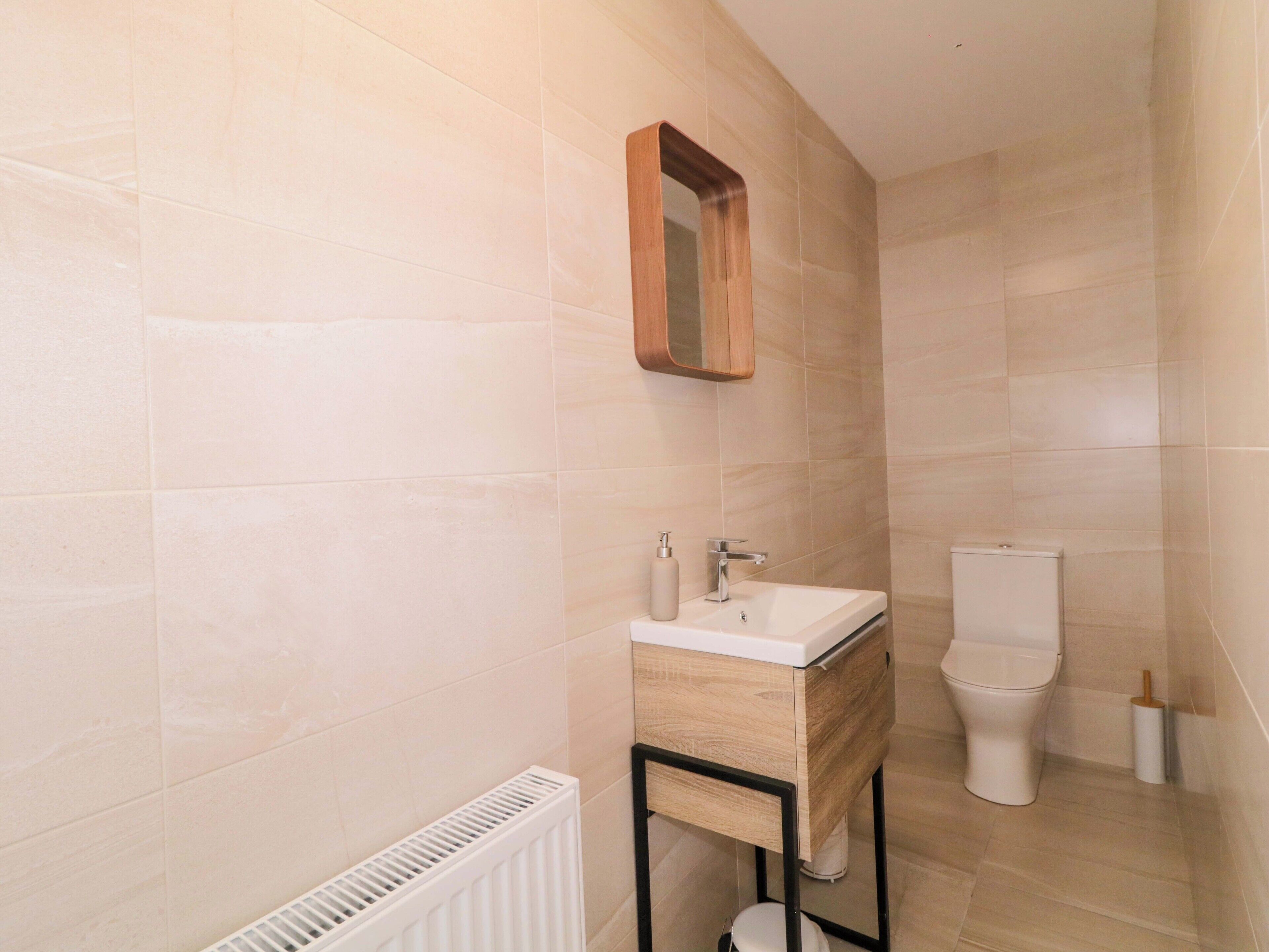 A bathroom with a wooden vanity, a white sink, a mirror, and a toilet.