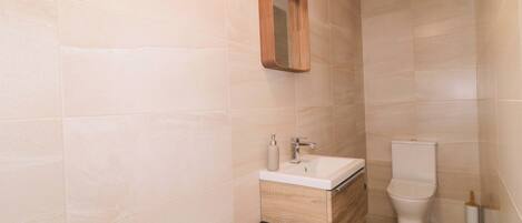 A bathroom with a wooden vanity, a white sink, a mirror, and a toilet.