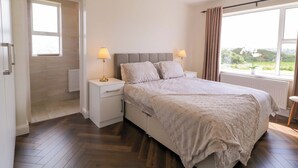 A bedroom with a bed, two bedside tables, a window with curtains, and a view of greenery outside. - ARD NA MARA, pet friendly, with open fire in Culdaff, County Donegal (Culdaff)