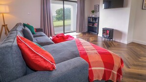 A living room with a sofa, a red blanket, a bookshelf, and a TV on the wall. - ARD NA MARA, pet friendly, with open fire in Culdaff, County Donegal (Culdaff)