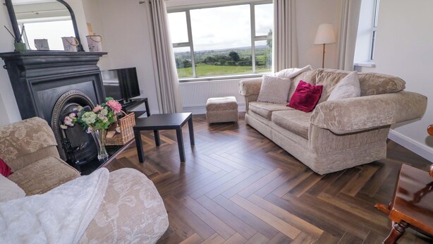 A living room with a fireplace, sofa, and a large window offering a view of the outdoors. - ARD NA MARA, pet friendly, with open fire in Culdaff, County Donegal (Culdaff)