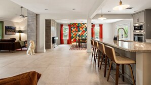 A modern kitchen with a central island, bar stools, and a dining area with a colorful wall. - Desert Disco - 4BR Mid-Century Modern Design (Austin)
