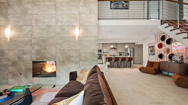 A spacious living area with a high ceiling, a fireplace, a modern kitchen, and a staircase leading to an upper level. - Desert Disco - 4BR Mid-Century Modern Design (Austin)