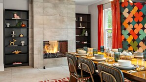 A modern dining area with a fireplace, black shelves with decorative items, and a colorful wall pattern. - Desert Disco - 4BR Mid-Century Modern Design (Austin)