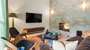 A modern living room with a flat-screen TV, a fireplace, and a glass coffee table. - Desert Disco - 4BR Mid-Century Modern Design (Austin)