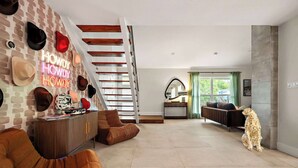 A spacious living room with a staircase, a sofa, a dog, and a wall with hats. - Desert Disco - 4BR Mid-Century Modern Design (Austin)