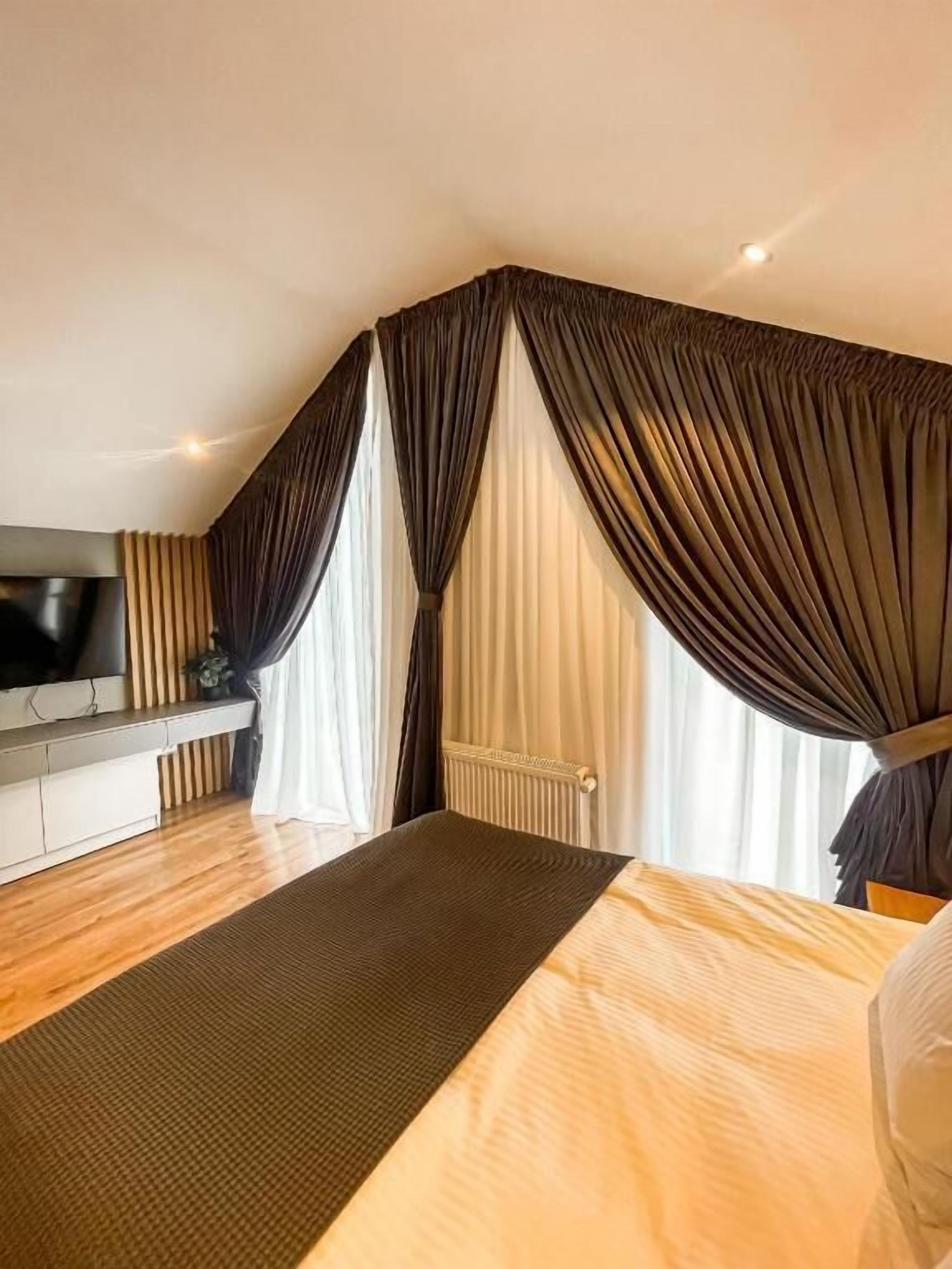Ein modernes Schlafzimmer mit einem großen Bett, einem Flachbildfernseher und einem großen Fenster mit dunklen Vorhängen.